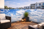 Custom-sized raster balcony screen with sky print, mounted on a terrace railing with garden furniture and a plant.