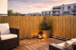 Custom-made bamboo balcony screening mounted on a terrace railing with garden furniture and a plant.