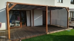 Cortina para cenador Premium de color gris instalada en una estructura de madera de una terraza junto a la casa.