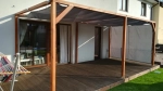Tenda da sole impermeabile su misura montata su una terrazza in legno con pergola e mobili da giardino.