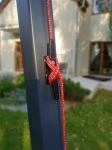 Corda vermelha enfiada através de um cunho de fixação preto montado num poste cinzento no jardim.