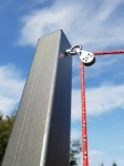 Cunho de metal prateado com polia montado num poste de aço, com uma corda vermelha sobre o fundo do céu azul.