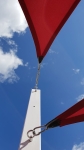 Tendeur en acier inoxydable tendant une voile d'ombrage rouge fixée à un poteau blanc.
