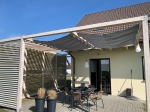 Vandtæt udtrækkeligt solsejl efter mål, monteret på en træpergola over en terrasse med møbler.