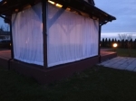 Perdea de terasă tip pachet care protejează un foișor de grădină la amurg.