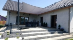 Custom-made waterproof sun sail mounted over a terrace with garden furniture at a detached house.