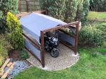 Toldo vela gris impermeable a medida titanio, que protege una moto bajo un cobertizo de madera.