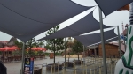 Toldo vela cuadrado gris impermeable premium 3x3m extendido sobre un camino en un parque de atracciones.