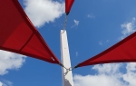 Tre angoli di una vela ombreggiante rossa premium montati su un palo bianco su sfondo cielo.