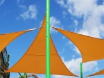 Orangefarbenes Premium-Sonnensegel wasserdicht 3x3x4,2 an einem grünen Mast vor blauem Himmel.