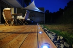 Terrasse en bois éclairée de nuit avec mobilier de jardin et voile d'ombrage triangulaire premium 3,5x3,5x3,5.