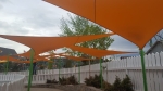 Waterdicht premium schaduwdoek 3,5x3,5x3,5 m in oranje boven een wit hek en groene struiken.