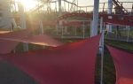 Red triangular premium waterproof sun sail 3.5x3.5x3.5 mounted over a path in an amusement park.