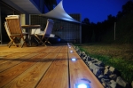 Vela ombreggiante triangolare impermeabile premium 5x5x7 che copre una terrazza in legno con mobili e luci d'atmosfera.