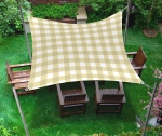 Waterproof 3x3 m garden sun sail in beige check, suspended over wooden chairs on green grass.