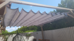 Grey horizontal premium Decor roman blind made to measure mounted on a wooden pergola in the garden.
