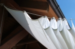 White waterproof retractable sail 3x3 m mounted on cables under a wooden terrace roof.