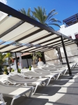 Witte Romeinse zonneschermen op een donkerhouten pergola boven rijen ligbedden bij het zwembad.