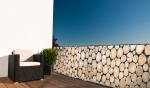 Balkonscherm op maat met boomstamprint, gemonteerd op een balkon met een fauteuil en een plant in pot.