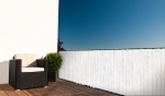 White balcony screen with wood print mounted on terrace railing next to a wicker chair and a plant.