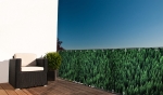 Balcony privacy screen with a coniferous forest print mounted on a terrace railing next to a woven armchair.