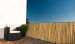 Custom-made bamboo balcony screen mounted on a terrace railing next to a dark armchair and a potted plant.