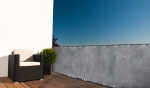 Grey custom-made balcony screen with print, installed on a terrace railing next to a polyrattan armchair.