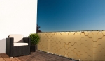 Golden balcony privacy screen with a honeycomb pattern, mounted on a terrace railing with garden furniture.