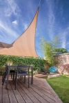 Beige triangular HDPE sun sail made to measure, mounted over a terrace with garden furniture.
