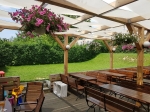Gazebo solar shade sail 1x5 m mounted on a wooden pergola in a summer garden with benches and flowers.