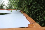 White custom-made gazebo sunshade strip, fixed with elastic ties to a wooden structure.