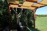 Custom-made brown HDPE sun shade sail strip mounted on a wooden pergola in a garden.