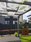 Grafische Sonnenschutz-Stoffbahn mit Blattmotiv, maßgefertigt unter einer modernen Pergola-Konstruktion.