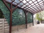 Tenda velata su misura con grafica a foglie, montata sotto una tettoia in legno come protezione laterale.