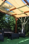 Beige HDPE schaduwstroken 0,5x5 m gemonteerd op een houten pergola boven tuinmeubelen op een zonnige dag.