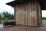 Cortina a medida con diseño de bambú instalada en la terraza de un cenador junto a una jardinera de madera.
