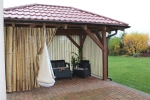 Cortina de terraço com padrão de bambu a proteger móveis de jardim num gazebo com chão de tijolo.