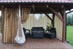 Maßgeschneiderter Vorhang mit Bambusgrafik, der einen Gartenpavillon mit Gartenmöbeln und Hängesessel abschirmt.