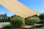 Toldo vela beige HDPE 4x4 extendido sobre el jardín proporciona sombra y un aspecto moderno a la terraza.
