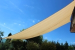 Voile d'ombrage carrée beige en HDPE 5x5 tendue dans un jardin sur fond de ciel bleu.