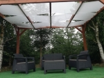 Copertină albă pentru foișor montată pe o pergolă din lemn deasupra unui set de mobilier de grădină.