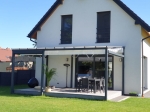 Οριζόντια premium ρωμαϊκή κουρτίνα Decor 2,5x3 τοποθετημένη σε μοντέρνα βεράντα με πέργκολα δίπλα σε λευκό σπίτι.
