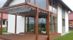 Store romain horizontal premium Decor 2,5x3 m installé sur une pergola en bois au-dessus de la terrasse d'une maison moderne.