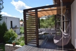 Store romain horizontal premium Decor 2,5x3 protégeant une terrasse avec meubles de jardin et fauteuil suspendu.
