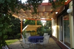 Μπεζ οριζόντια ρωμαϊκή κουρτίνα premium Decor 2,5x3 τοποθετημένη σε ξύλινη πέργκολα πάνω από βεράντα με έπιπλα.