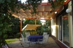 Store romain horizontal premium Decor 2,5x3 beige monté sur une pergola en bois au-dessus d'une terrasse avec meubles.
