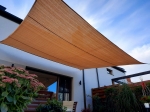 Zandkleurig vierkant HDPE schaduwdoek 3x3 m gemonteerd boven het terras van een moderne woning met tuin.
