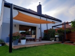 Oranje HDPE schaduwdoek 3x3 m gemonteerd boven een terras met tuinmeubelen en planten in potten.