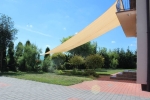 Vela ombreggiante triangolare in HDPE sabbia 3x3 montata sopra una terrazza in un giardino soleggiato.