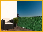 Groen raster balkon privacyscherm op maat gemonteerd op een terrasleuning met een donkere fauteuil en plant in pot.